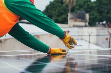 A solar technician working on the installation of solar panels on a rooftop with focus on tools and safety gear.